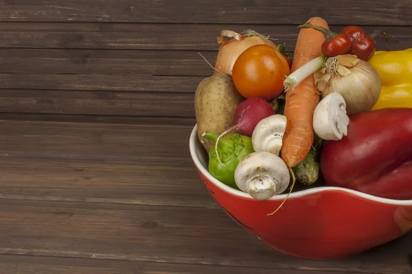 Vegetables in a red bowl on the table, instead of text. Various types of vegetables on an old wooden table. The concept of diet food. Food for obese patients. Autumn harvest vegetables.