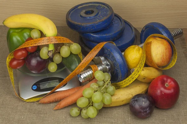 Chrome dumbbells surrounded with healthy fruits and vegetables on a table. Concept of healthy eating and weight loss. Diet for athletes.