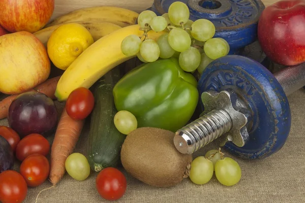 Chrome dumbbells surrounded with healthy fruits and vegetables on a table. Concept of healthy eating and weight loss. Diet for athletes.