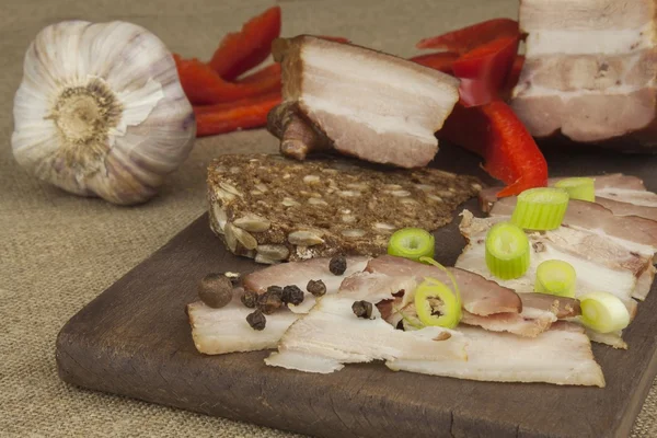 Preparing home-made snacks for the guests. Cutting board with smoked bacon and bread. Raw bacon. Whole grain bread.