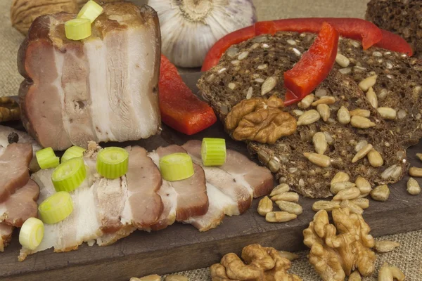 Preparing home-made snacks for the guests. Cutting board with smoked bacon and bread. Raw bacon. Whole grain bread.