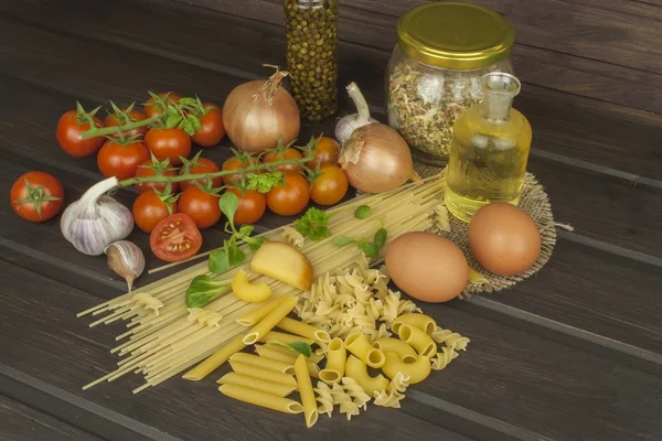 Preparing homemade pasta. Pasta and vegetables on a wooden table. Dietary food. Pasta, tomatoes, onion, olive oil and basil on wooden background.