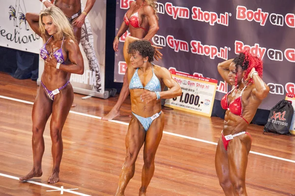 Three female bodybuilders in abdominals and thighs pose in lineu