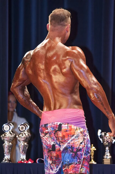 Male physique contestant shows his best back pose on stage