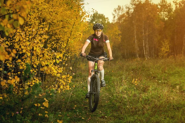 Woman biking in yellow autumn forest on a meadow