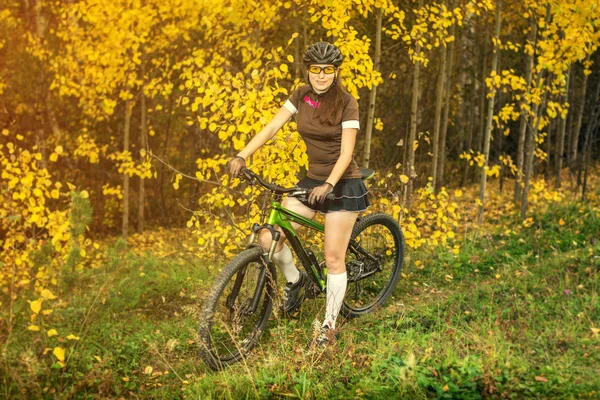 Woman biking in yellow autumn forest on a meadow