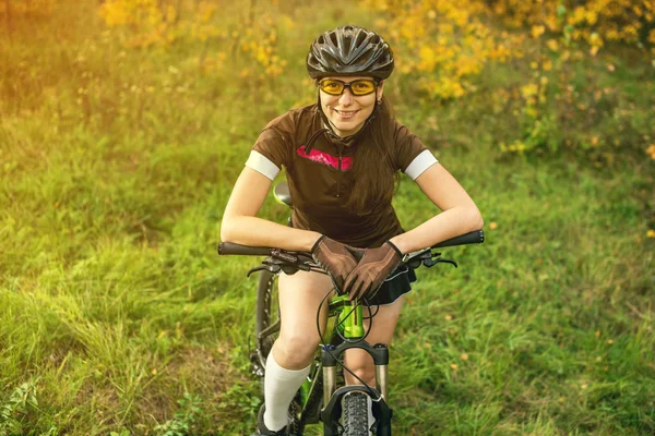 Woman biking in yellow autumn forest on a meadow