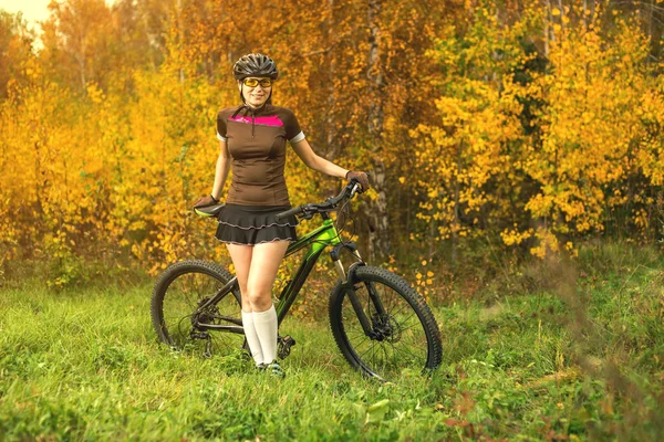 Woman biking in yellow autumn forest on a meadow