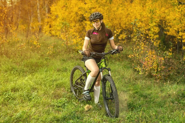 Woman biking in yellow autumn forest on a meadow