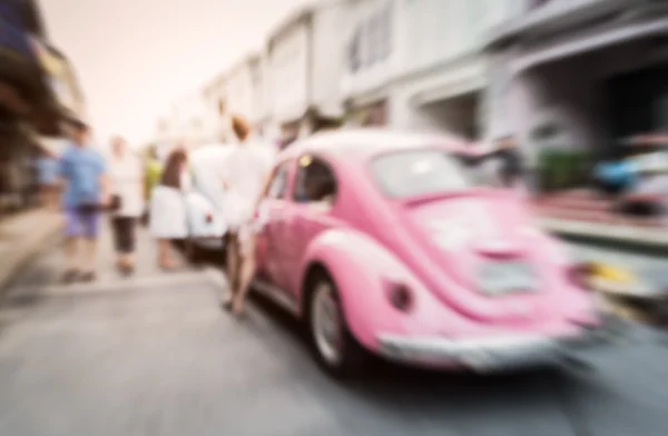 Blurred pink car on the road with people