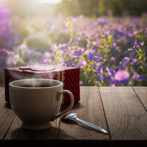 Hot coffee and gift box on wooden table in the meadow
