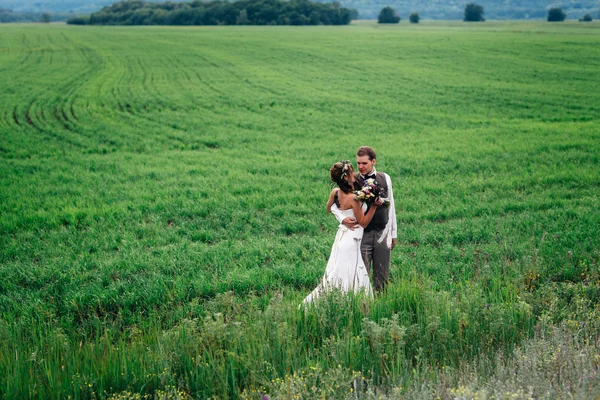 The bride and groom with a bouquet on the green field