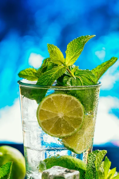 Glass of mojito with lime and mint ice cube close-up red straw on blue background