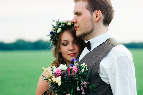 Portrait of the bride and groom with a bouquet on the green field