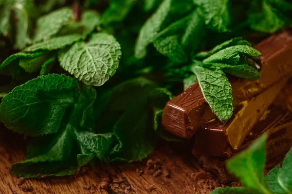 Stack of chocolate pieces with a leaf of mint on wooden background