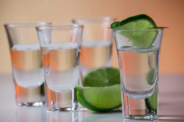 Tequila shot with a slice of lime on the glass orange background