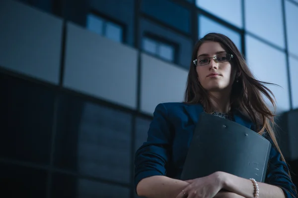 Successful beautiful young business woman standing against a background of buildings and holding folder.