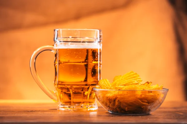 Light beer mug with a bowl of potato chips on a wooden table
