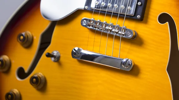 Electric jazz guitar close up on an orange sunburst color and chrome electronics