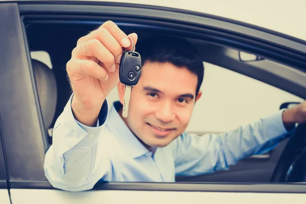 Smiling asian man as a driver showing car key  (key focused)