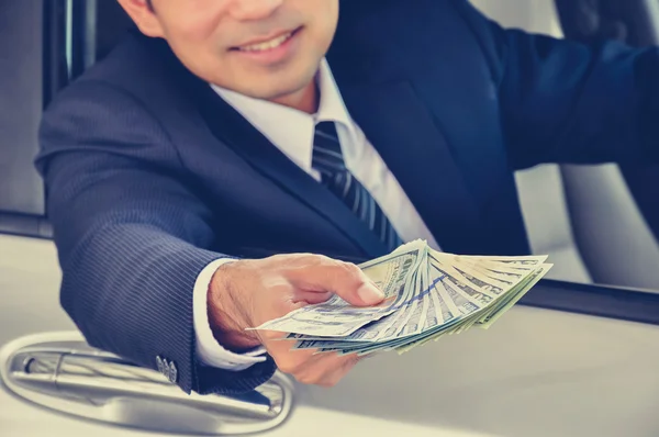 Business man giving money (US dollar bills) while sitting in a car