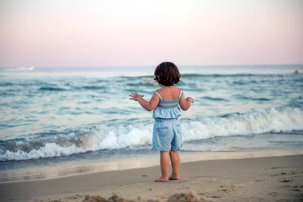 Little girl looks at the waves at sunset