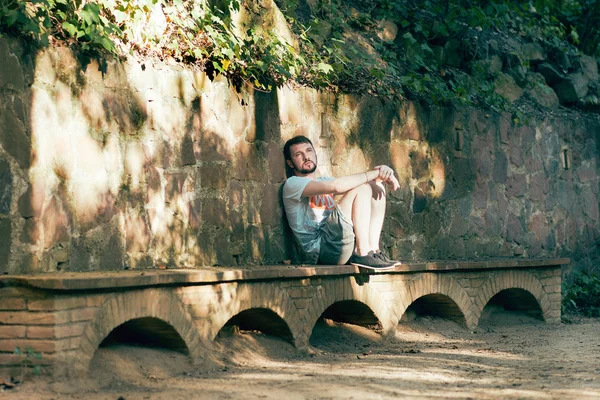 Handsome young man in a European city, sitting on a stone bench and thinks sad