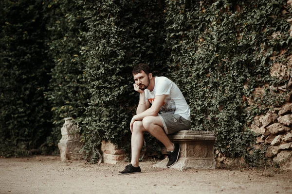 Handsome young man in a European city, sitting on a stone bench and thinks sad
