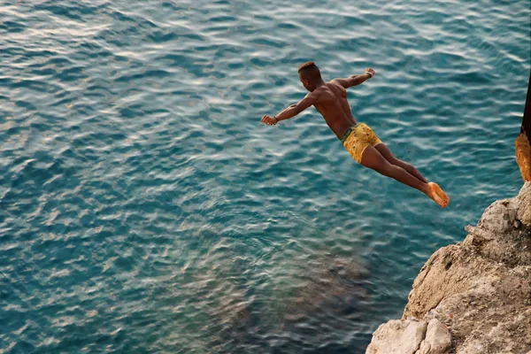 Young man jumping from cliff into sea.