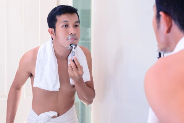 Young handsome man shaving by oneself with mirror.