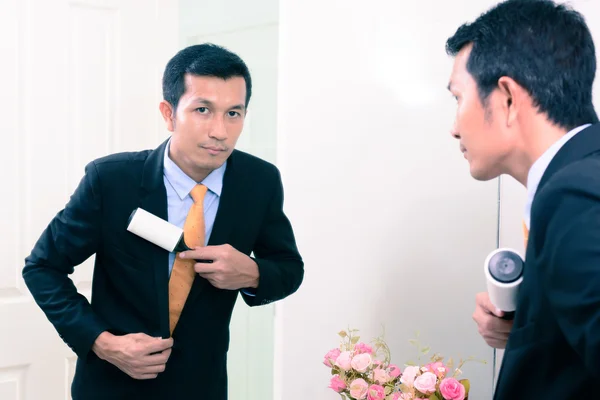 Businessman in black suit use a sticky brush to cleaning clothes from dust at dressing room.