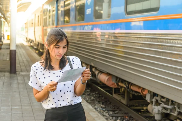 Woman watching a ticket before boarding the train at platform.