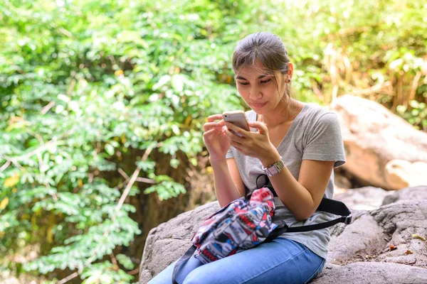 Woman with mobile phone have rest on stone in forest.