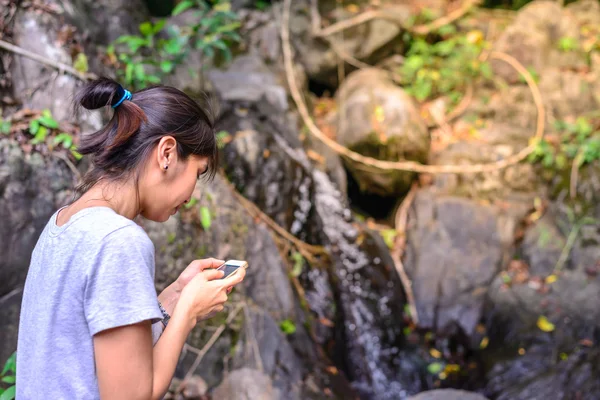 Woman with mobile phone have rest on stone in forest.