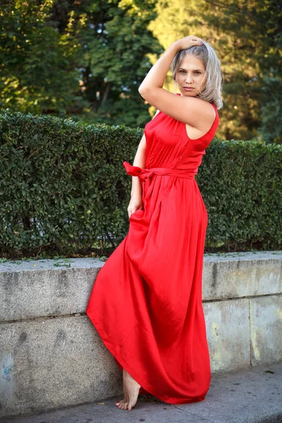 Beautiful girl posing in a red evening dress in the park outdoor