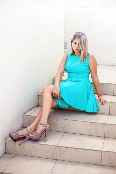 Young beautiful girl in a turquoise sundress posing on the steps