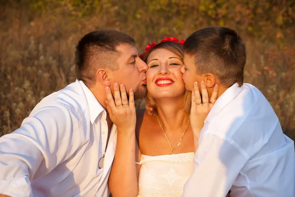 Dad and son kissing his mother on the cheek on both sides, in th