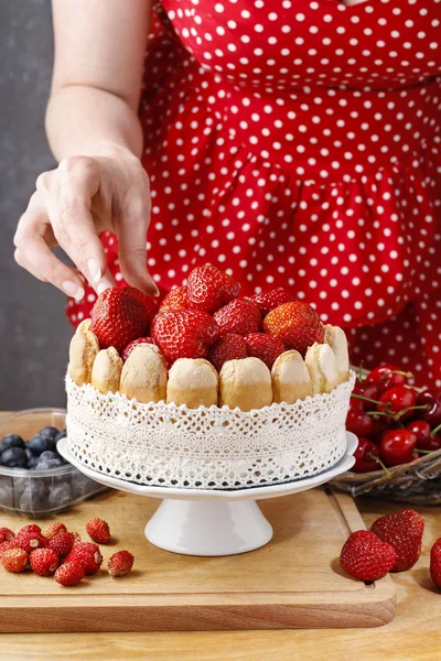 Woman holding summer sponge cake with fruits on ceramic cake sta