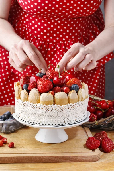 Woman holding summer sponge cake with fruits on ceramic cake sta