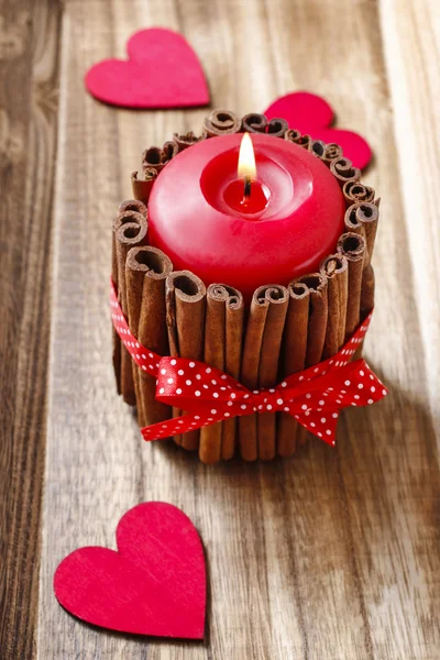 Red scented candle decorated with cinnamon sticks.