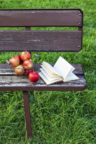 Book and apples on the bench in the garden
