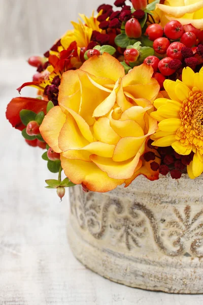 Bouquet of orange roses and autumn plants in vintage ceramic vas