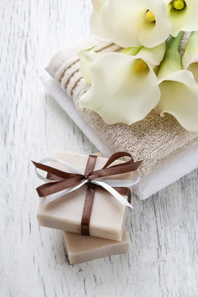 Bar of handmade natural soap, towels and bouquet of white calla