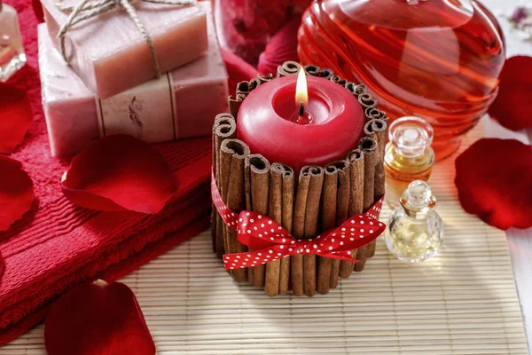 Red scented candle decorated with cinnamon sticks. Rose petals a