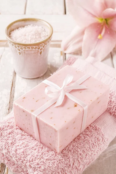 Bar of soap, bowl of sea salt, pink towel and lily flower