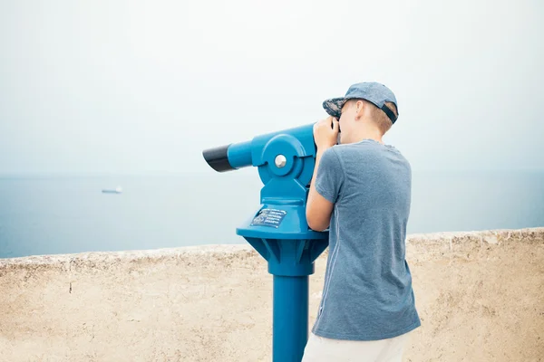 Teenager is looking through panorama binoculars telescope to the city beach.