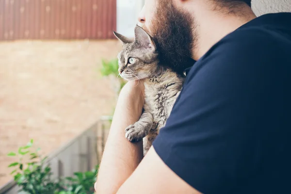 A man with a beard is hugging with his lovely Devon Rex cat