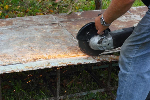 Worker cuts metal sheet by angle grinder