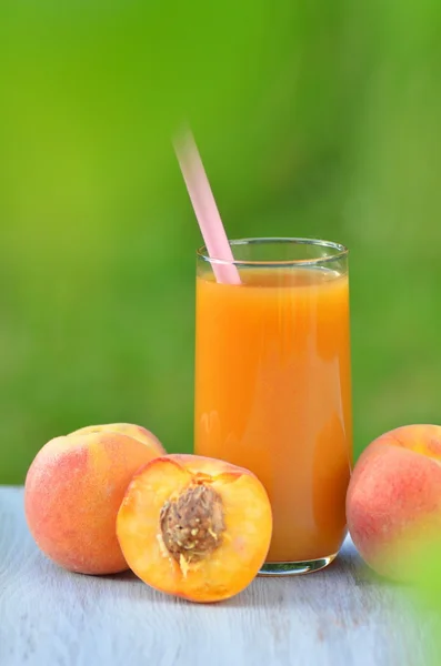 Glass of delicious peach juice and peaches on table in garden