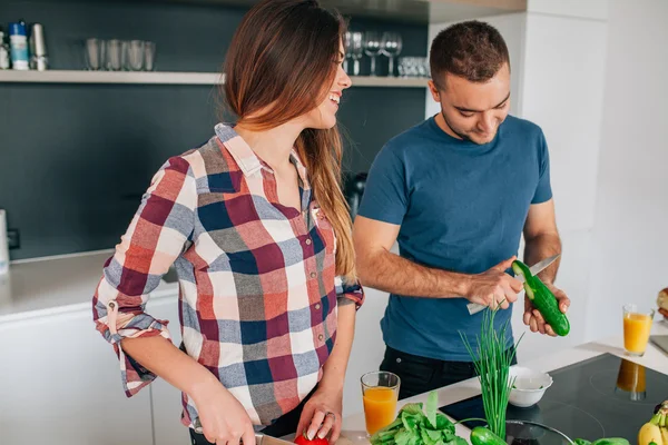 Young couple preparing salad in the kitchen. They are cutting to